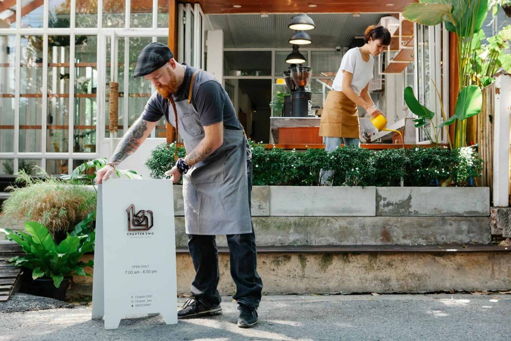 bearded man installing signboard while woman watering green plants